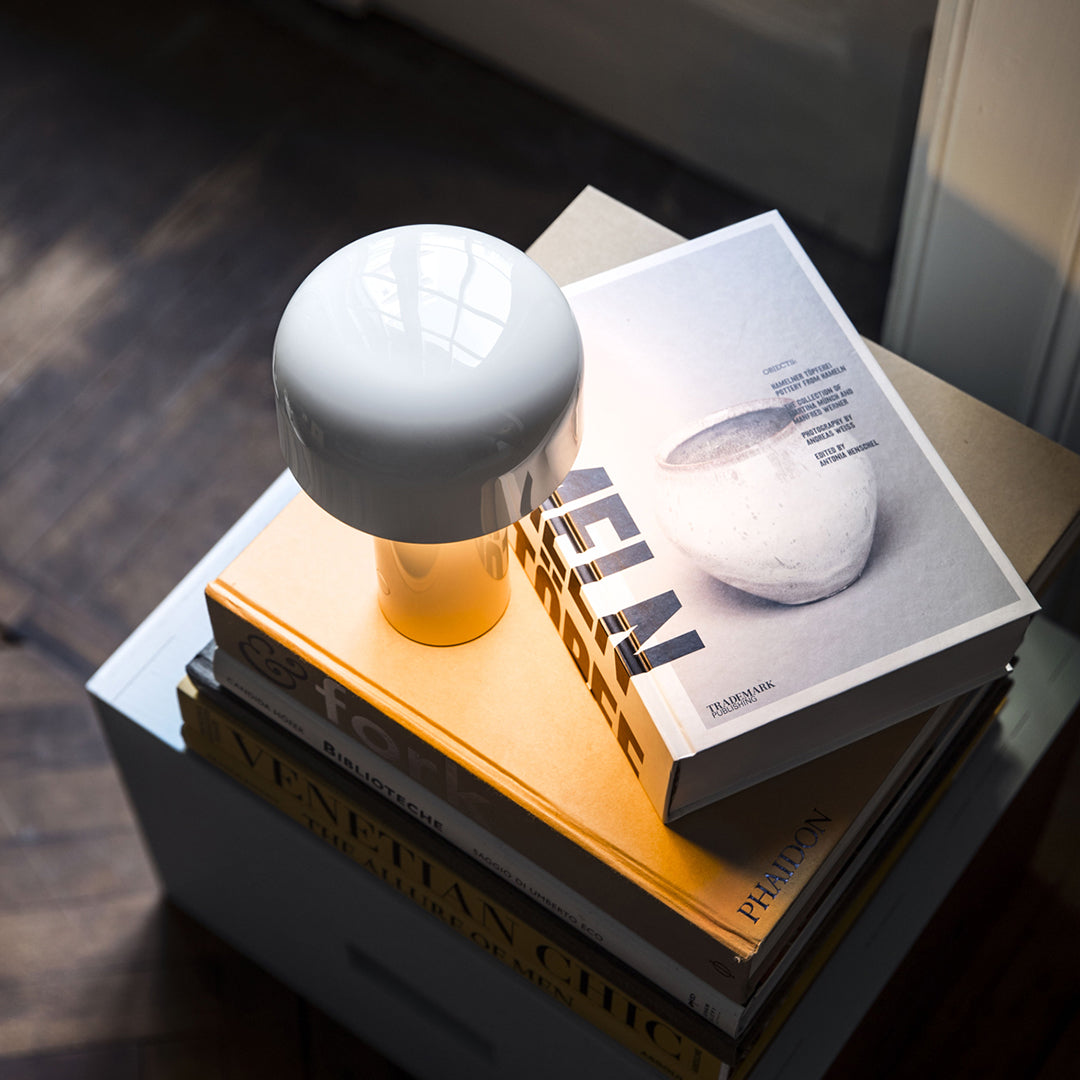 Glossy white lamp atop stacked books with yellow and gray covers, featuring modern minimalistic design.