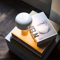 Glossy white lamp atop stacked books with yellow and gray covers, featuring modern minimalistic design.