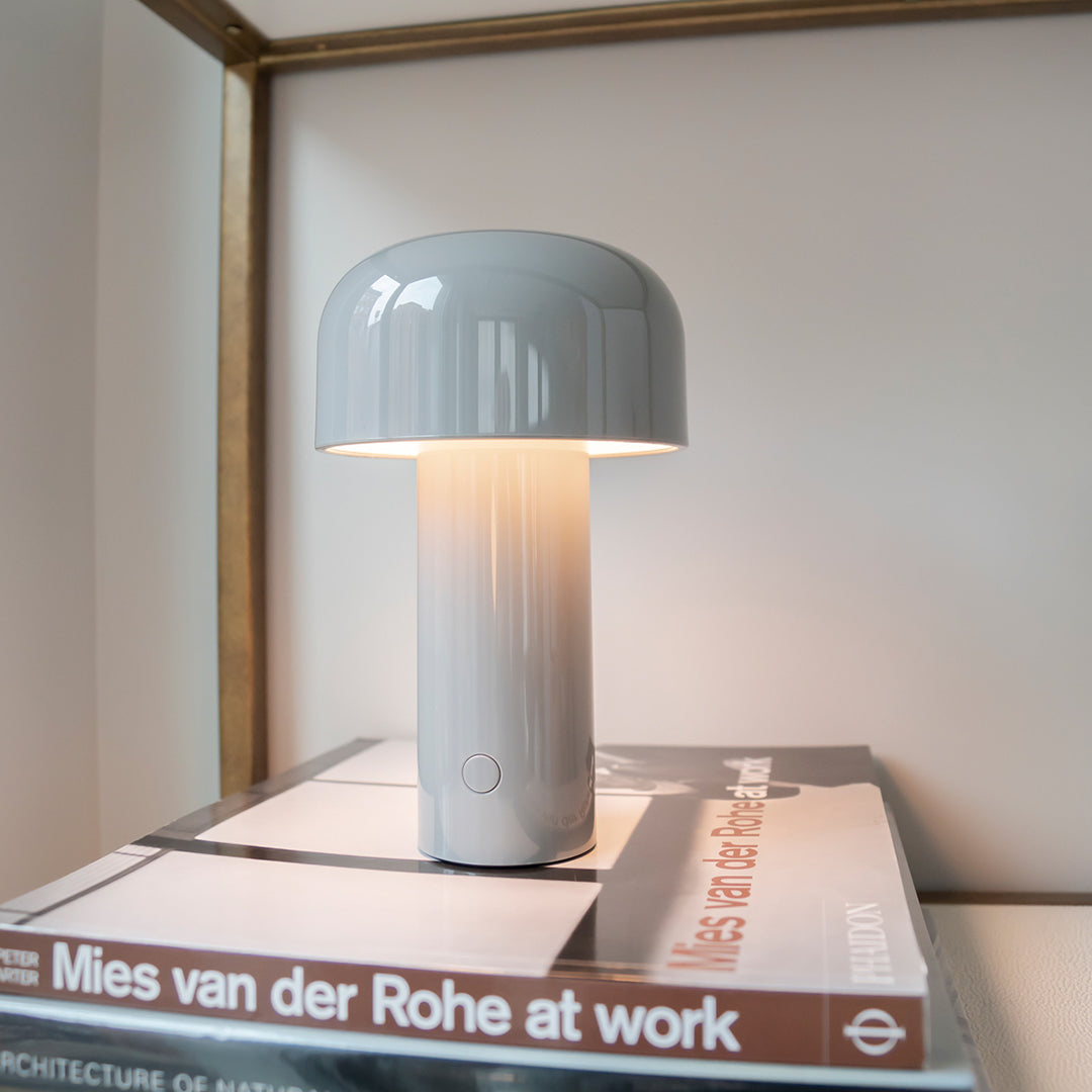 Gray ceramic lamp with a glossy finish and rounded top, placed on a stack of sleek, modern books.
