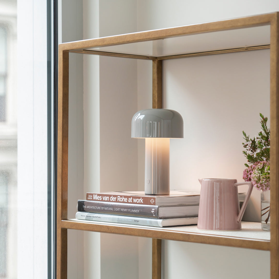 Gray mushroom lamp on books in a warm, neutral shelf setting with soft pink accents. Clean, modern design.