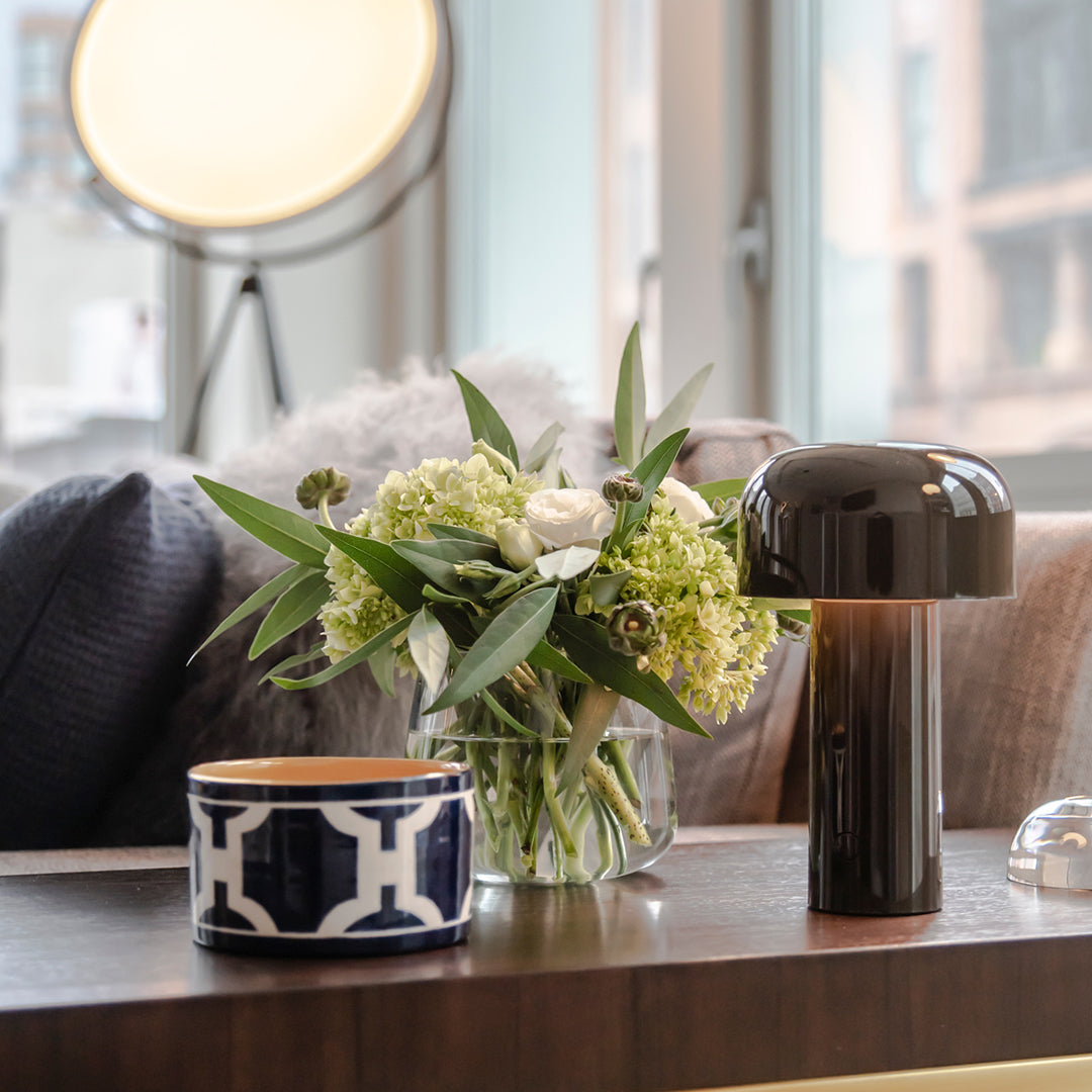 Stylish black lamp, geometric navy and white planter, and fresh greenery on a modern wooden table setting.