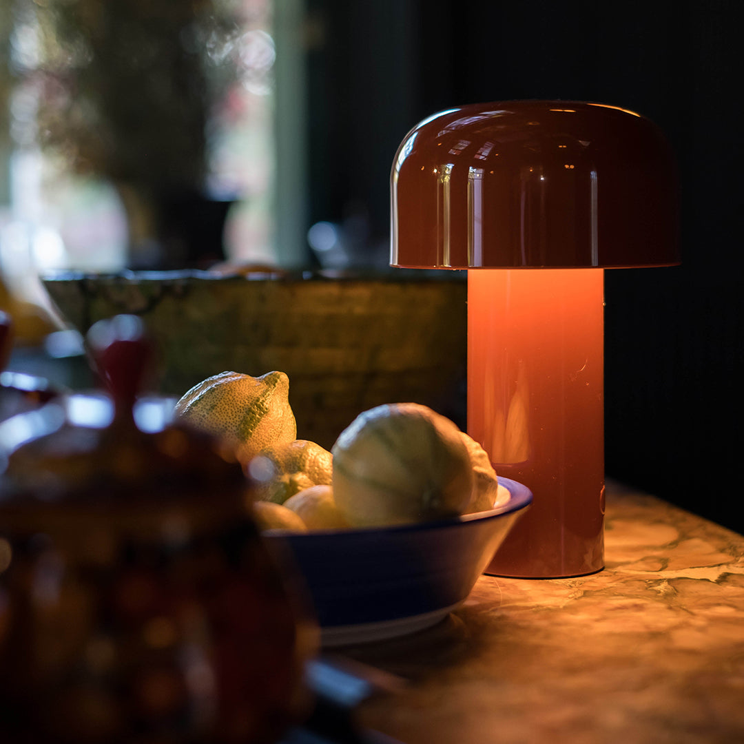 Brown mushroom-shaped lamp with a glowing orange light, set against a dark background and rustic tableware.