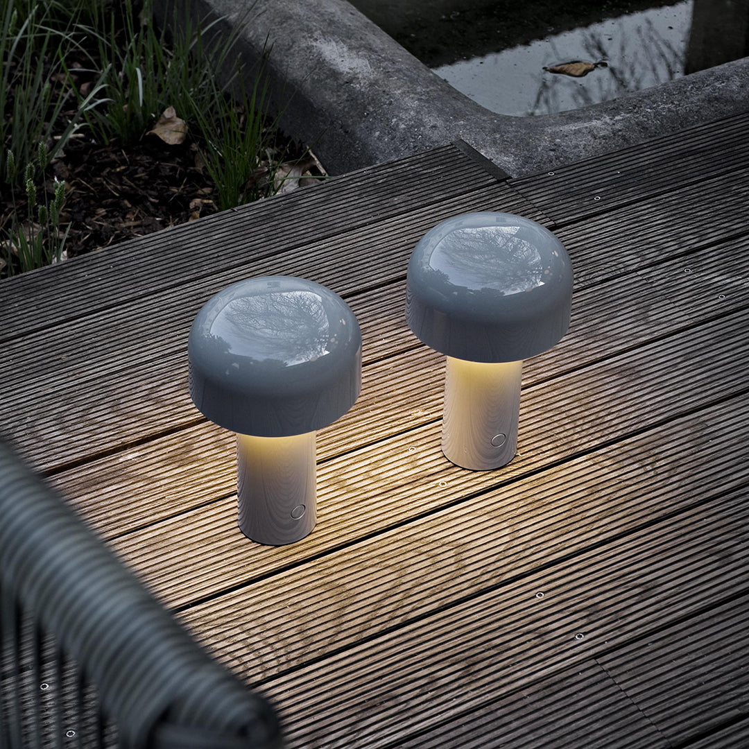 Two modern gray mushroom-shaped lamps with soft yellow glow, resting on a wooden deck with natural surroundings.