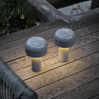 Gray mushroom-shaped outdoor lamps with smooth surfaces and soft glowing bases, set on wooden decking.