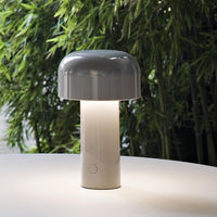 Modern gray mushroom lamp with a glossy finish and a white base, set against a lush green background.