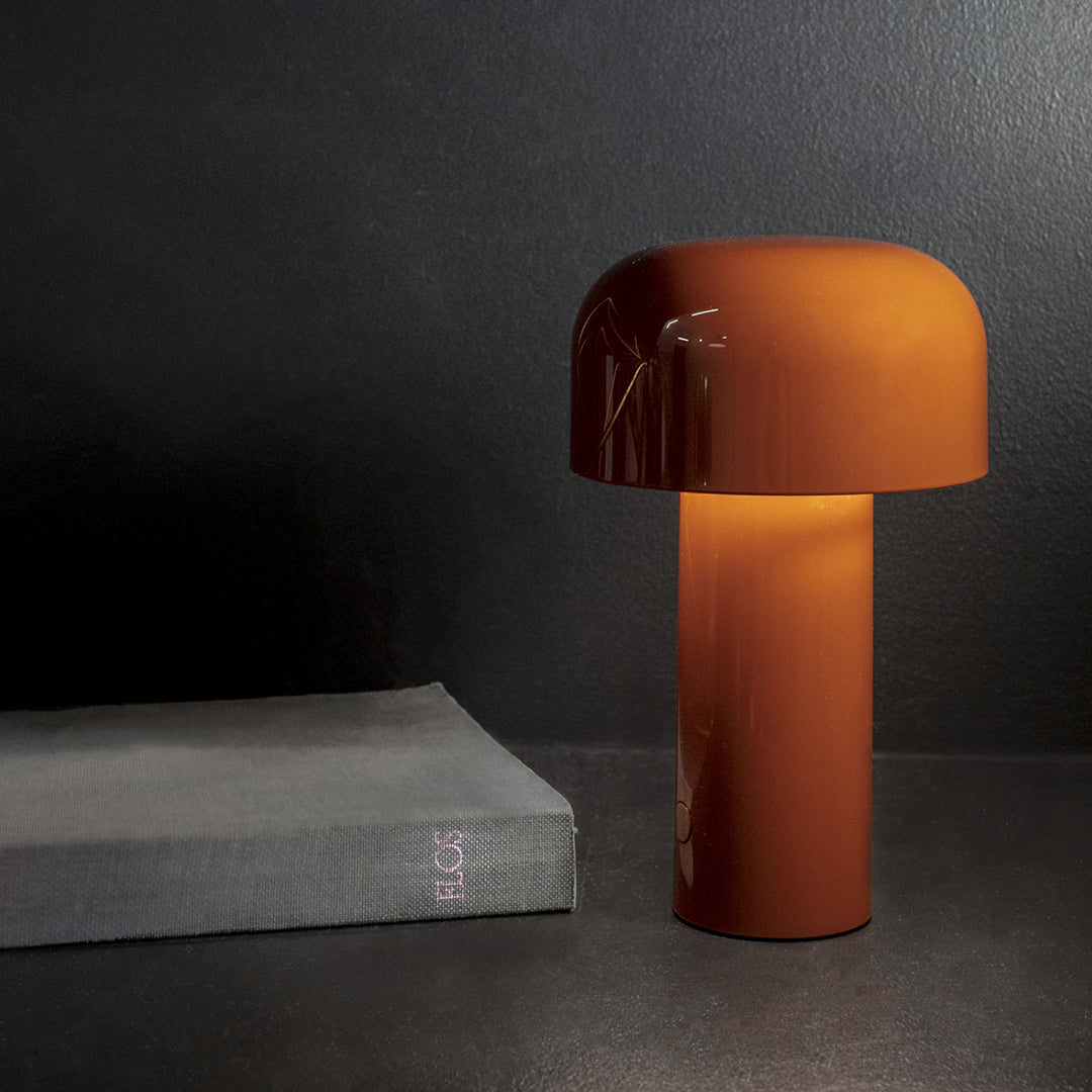 Glossy amber lamp with a mushroom shape on a dark background, complemented by a grey book.