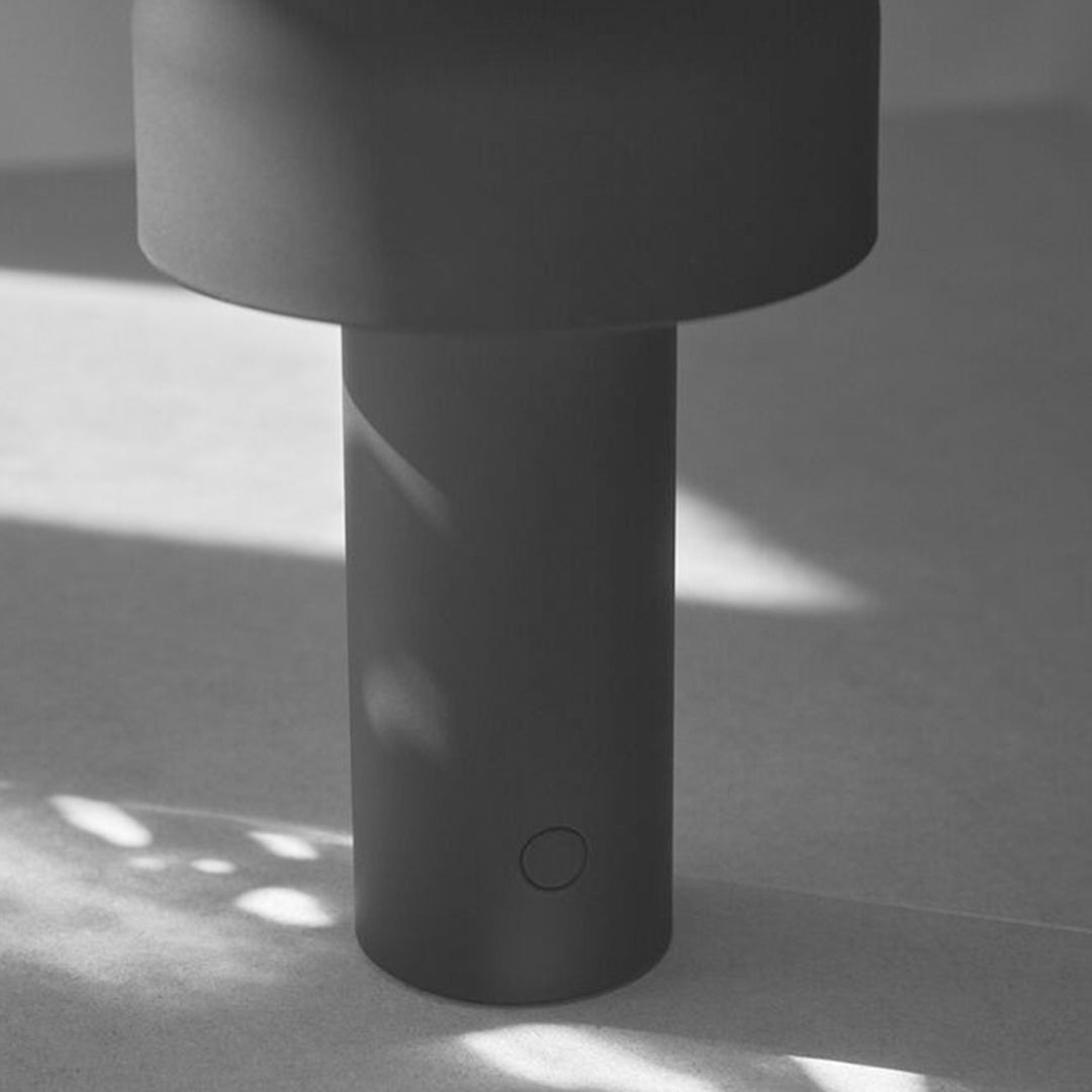 Modern matte black lamp with a cylindrical base and smooth, minimalist design, featuring subtle shadows and light play.