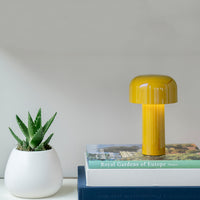 Yellow mushroom-shaped lamp on stacked books with a white planter and green succulent. Modern, minimalist design.