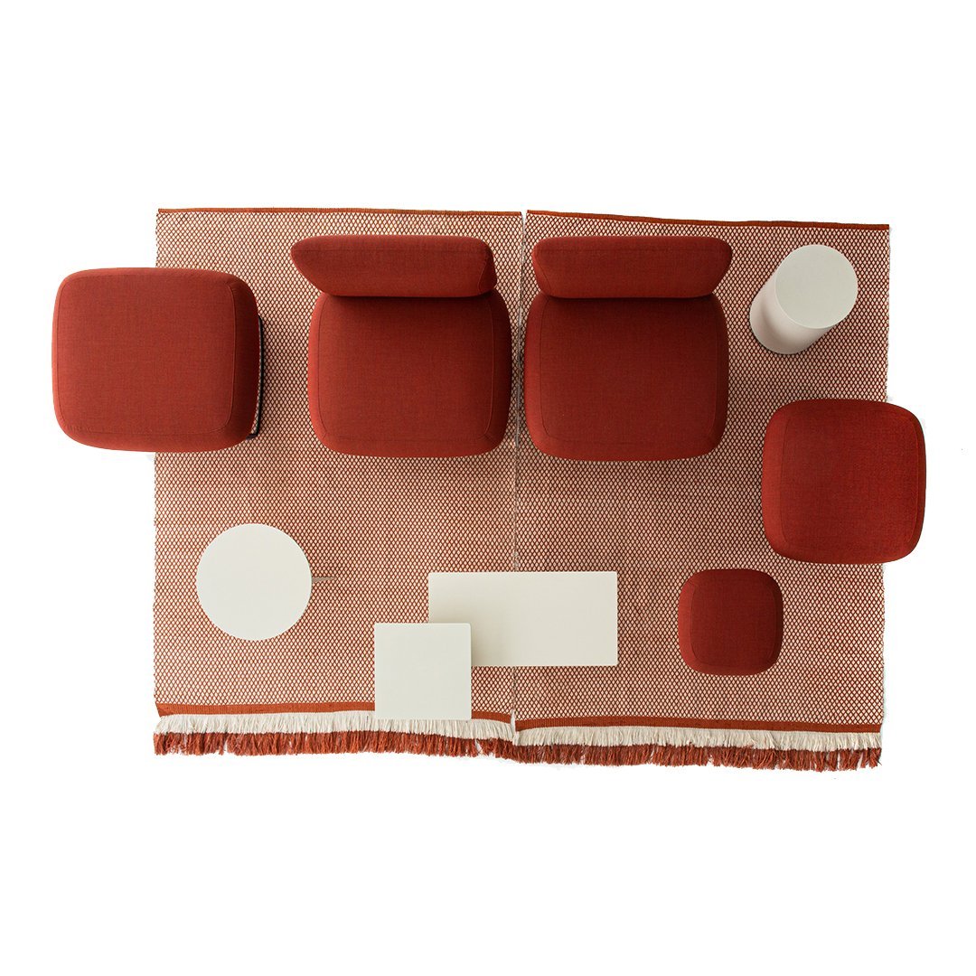 Top view of modern seating in rich red tones over a textured, woven rug with a soft beige and white accent.