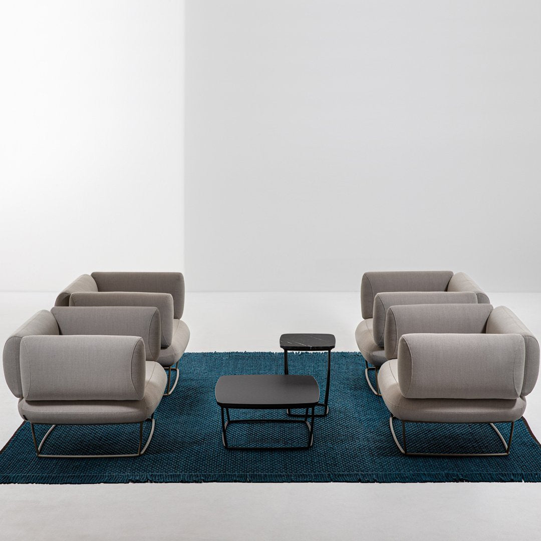 Gray armchairs on a textured blue rug with a sleek black coffee table, featuring modern, minimalist design elements.