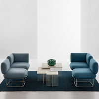 Blue and teal couches on a dark blue rug with a modern, geometric table and green decorative item.