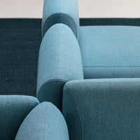 Blue upholstered sofa with a textured surface and smooth, rounded armrests, paired with dark textured rug.