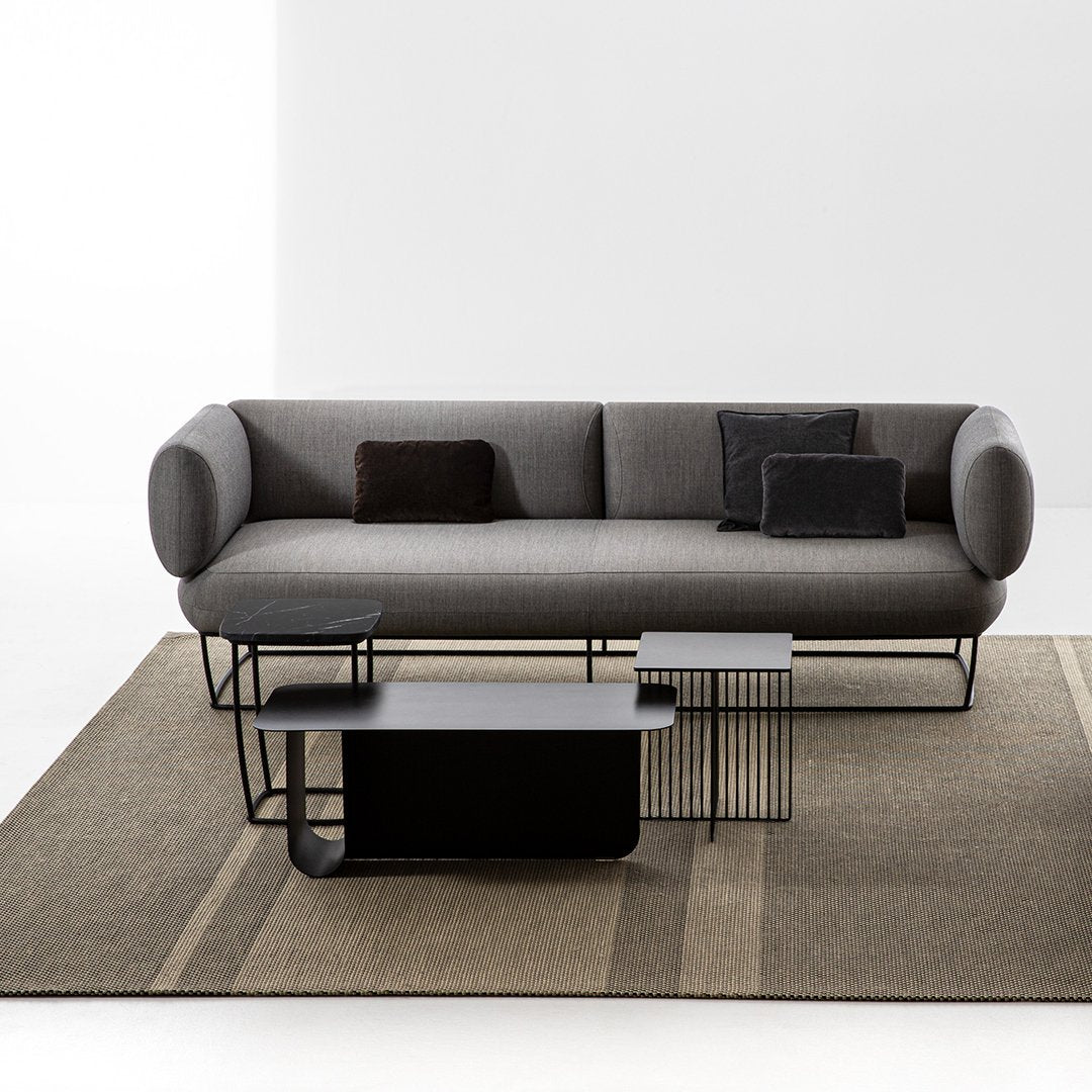 Gray modern sofa with black accent pillows and sleek black coffee tables on a textured beige and brown rug.
