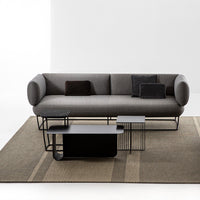 Gray modern sofa with black accent pillows and sleek black coffee tables on a textured beige and brown rug.