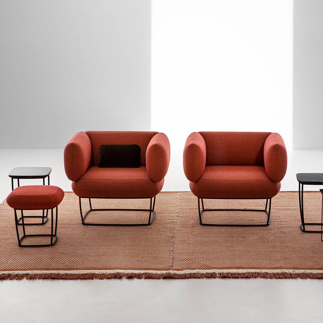 Rust orange armchairs with circular backs, set on a textured brown rug, paired with black and red accent tables.