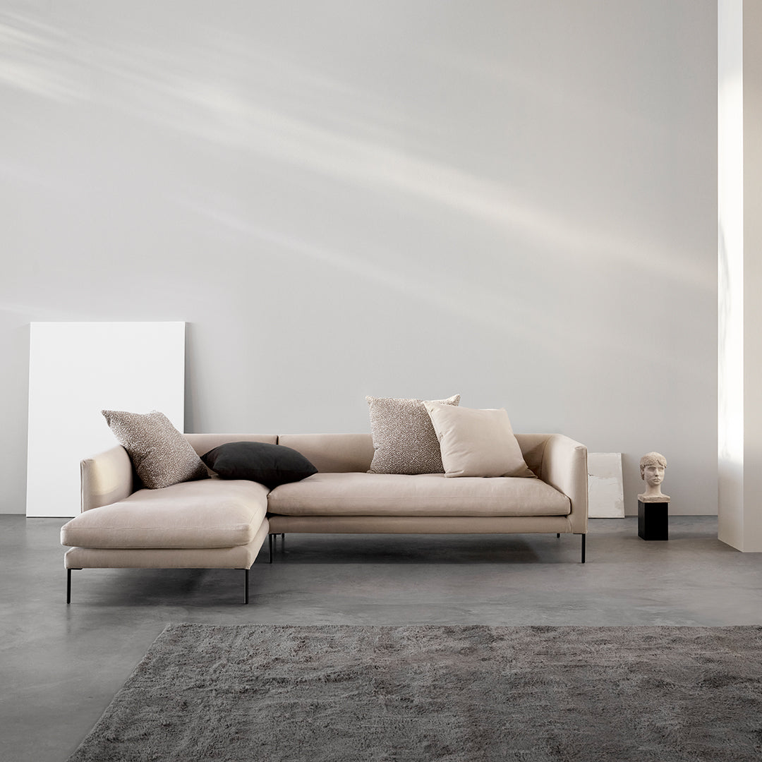 Beige sectional sofa with textured cushions, set against a minimalist gray backdrop and soft rug.