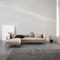 Beige sectional sofa with textured cushions, set against a minimalist gray backdrop and soft rug.