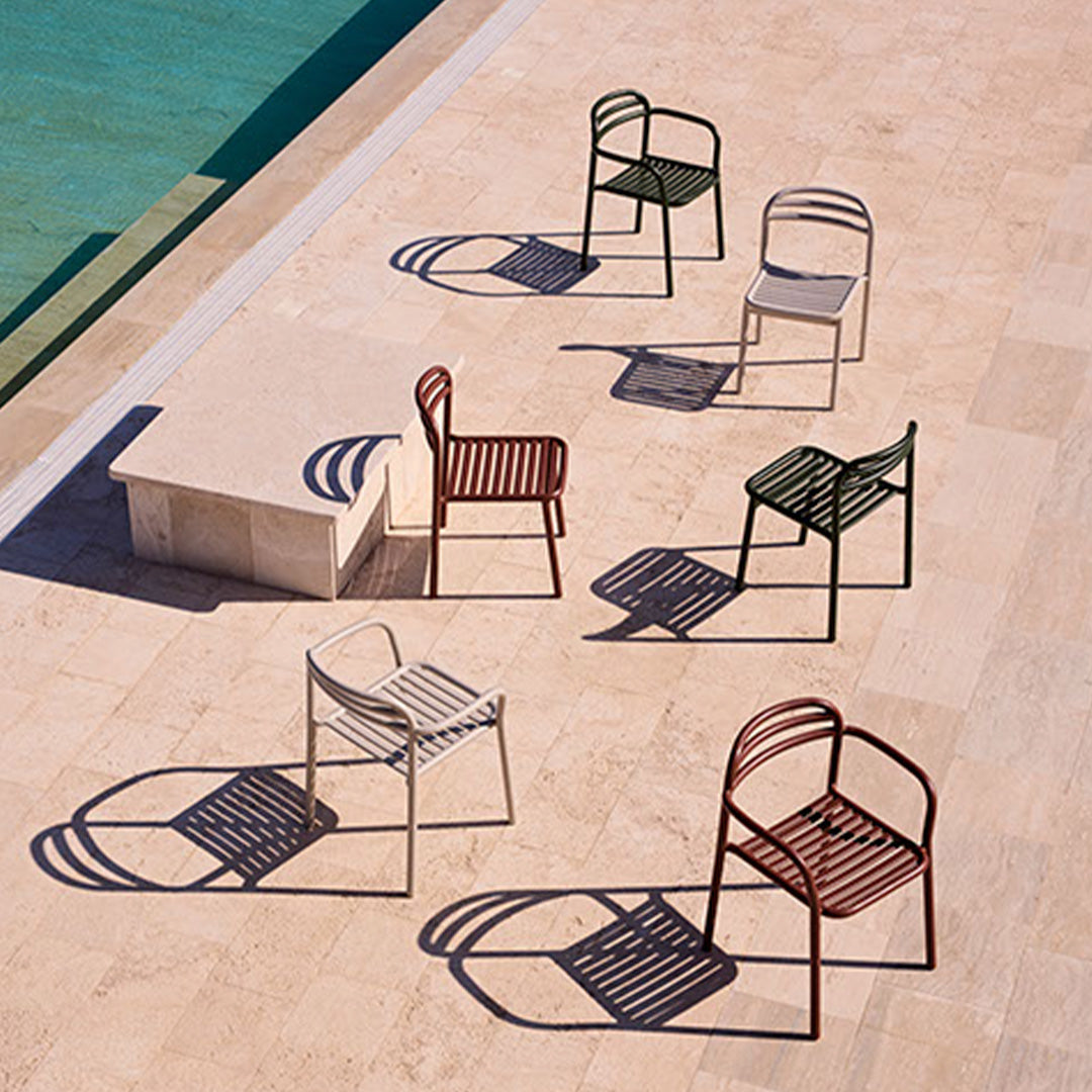 "Collection of colorful chairs in green, red, gray, and white, casting shadows on a stone surface by a pool."