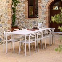 White outdoor dining table and chairs set against rustic stone wall, elegant and minimalistic design in a natural setting.