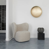 Cozy beige boucle chair with rounded shape, set against a minimalist white wall and gray herringbone floor.