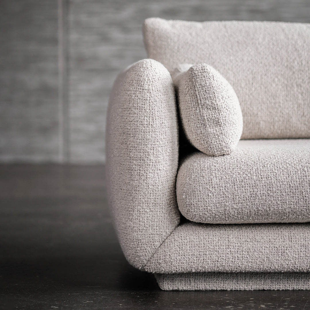 Textured cream-colored sofa with a plump armrest and round cushion, featuring a soft, cozy appearance.