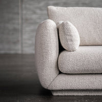 Textured cream-colored sofa with a plump armrest and round cushion, featuring a soft, cozy appearance.