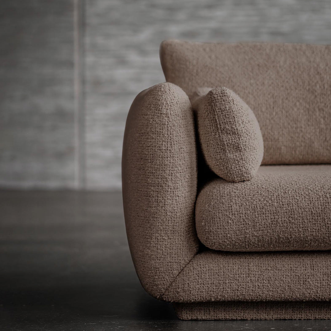Textured brown sofa with a rounded armrest and a plush, coordinating cushion against a neutral background.