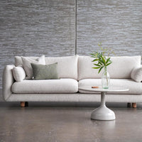 Light gray fabric sofa with textured pattern, accented by green throw pillow and a white round table. Modern minimalist decor.