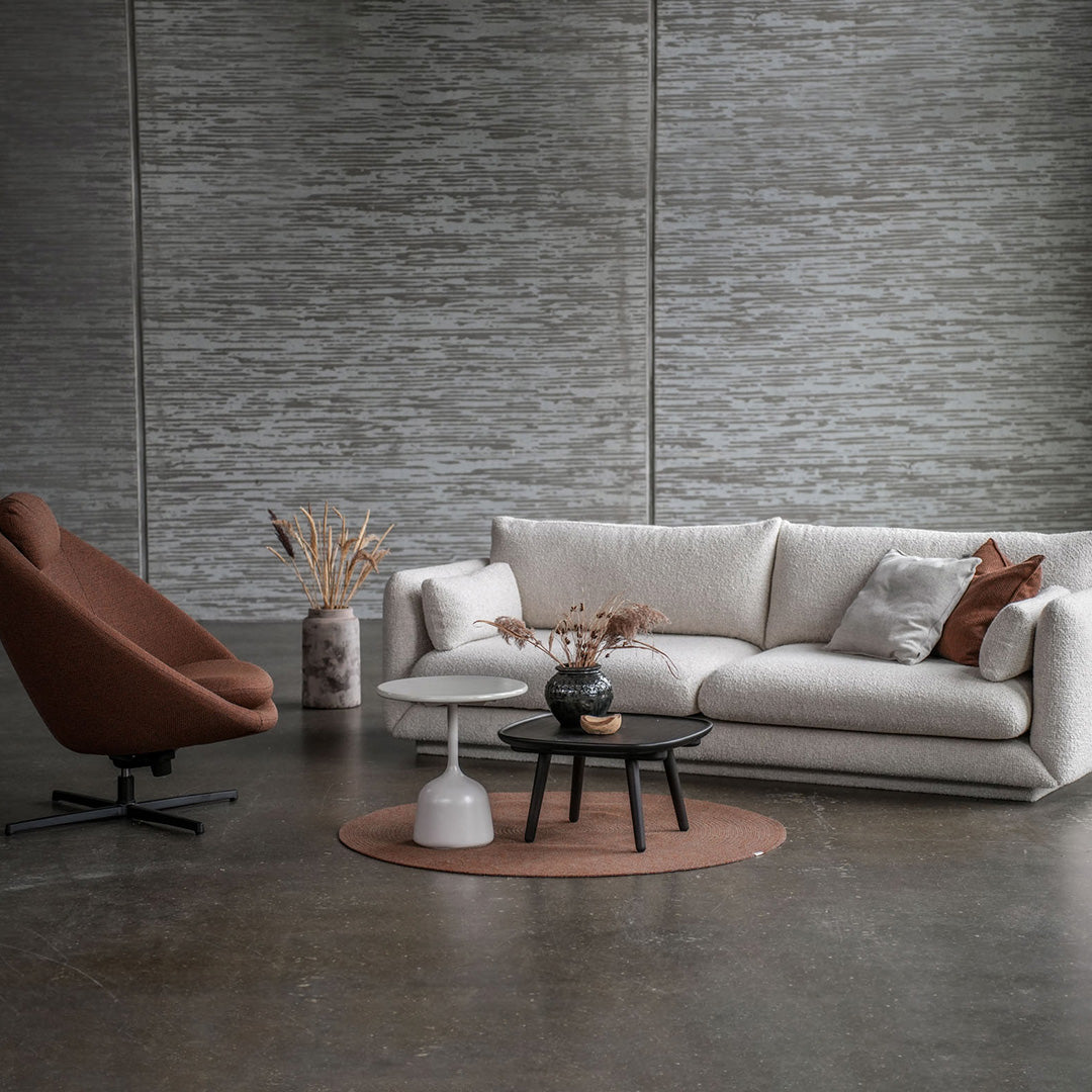 Light gray textured wall with a cream sofa, rust-colored chair, black coffee table, and muted brown accent rug.