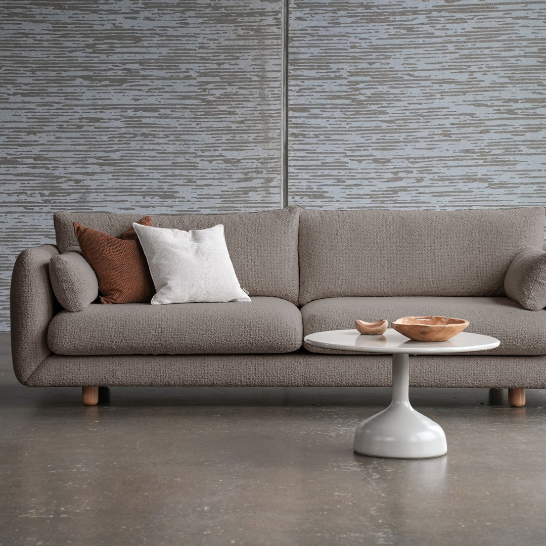 Textured gray sofa with brown and white accent pillows, paired with a round white coffee table. Minimalist design.