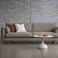 Textured gray sofa with brown and white accent pillows, paired with a round white coffee table. Minimalist design.
