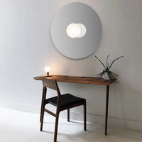 "Modern round mirror with soft gray tones and a minimalist wooden desk featuring a black chair and subtle plant accents."
