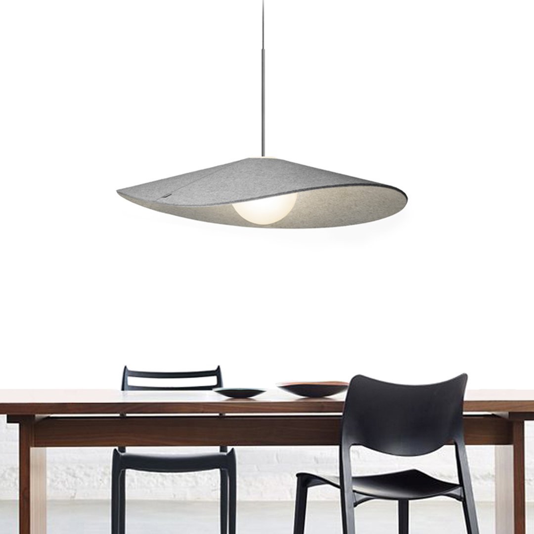 Gray hanging lamp with a sleek, geometric shape illuminating a modern wooden dining table and black chairs.
