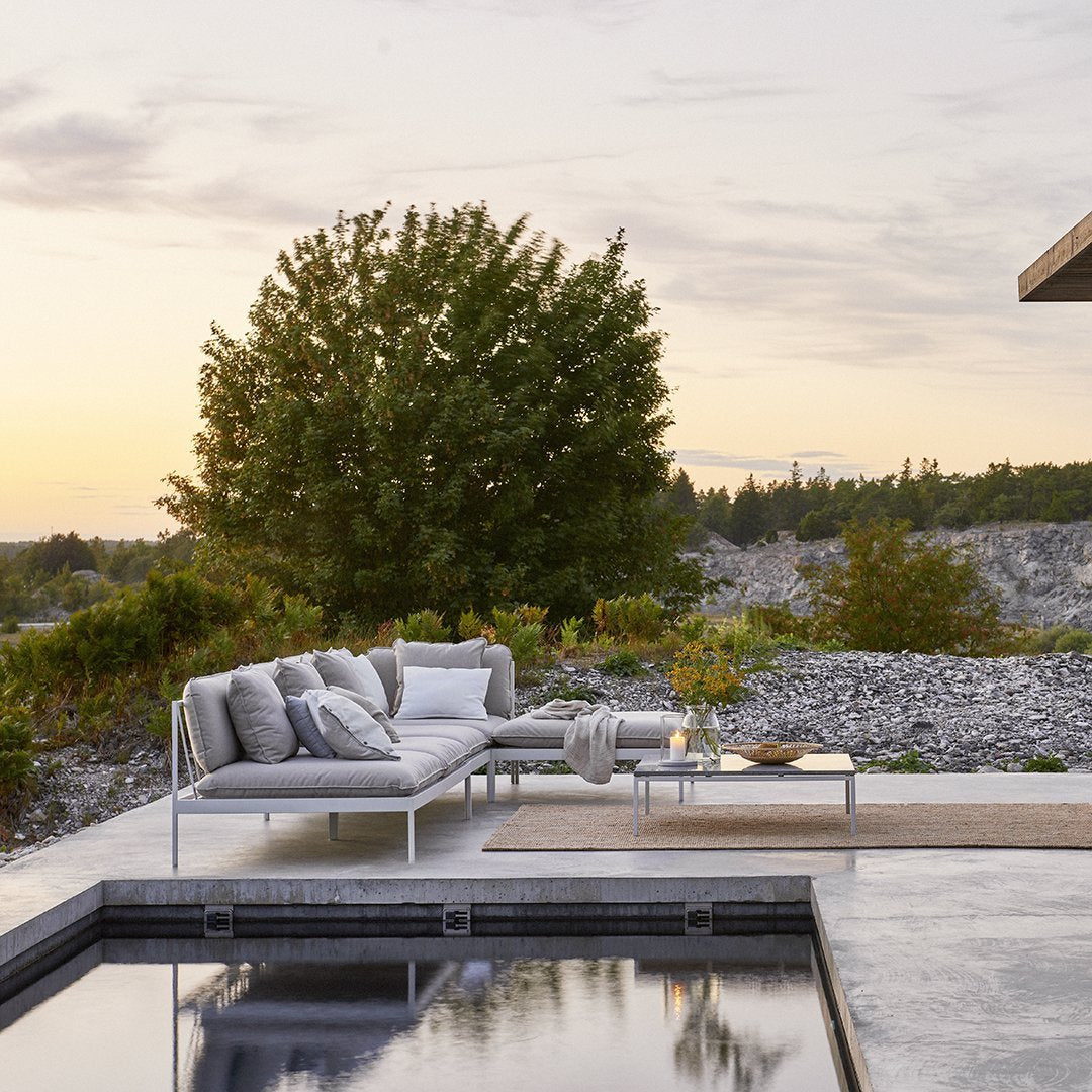 Modern outdoor sofa in gray fabric with mixed textures, set against a natural landscape at sunset.