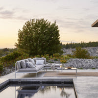 Modern outdoor sofa in gray fabric with mixed textures, set against a natural landscape at sunset.