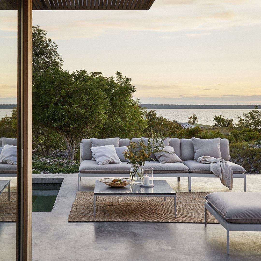 Light gray outdoor sectional sofa with soft white cushions, accompanied by a neutral-toned rug and glass coffee table.