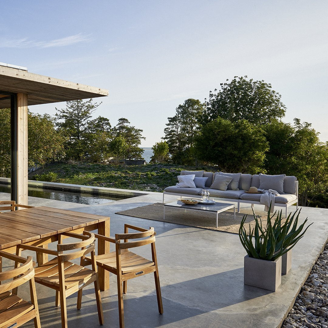"Neutral-toned sofa with light cushions, complementing warm wooden dining chairs, set against a natural landscape."