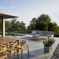 "Neutral-toned sofa with light cushions, complementing warm wooden dining chairs, set against a natural landscape."