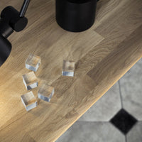 Clear glass cubes on a light wood table, contrasting with a black lamp and patterned floor tiles.
