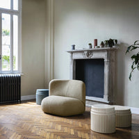 Neutral beige armchair and textured cream, light blue, and gray poufs against a warm wooden floor and soft wall colors.