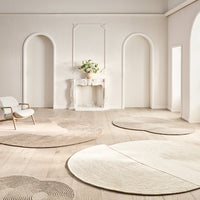 Minimalist round rugs in soft beige and cream tones with subtle circular patterns, complementing a neutral indoor space.