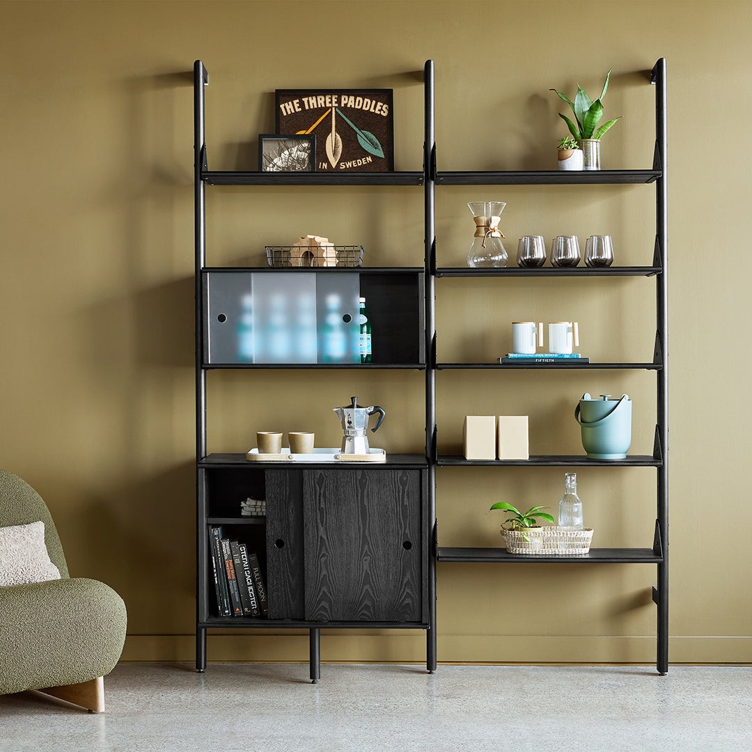 Black shelving unit against olive green wall, featuring clear and muted accents with natural wood and metallic elements.