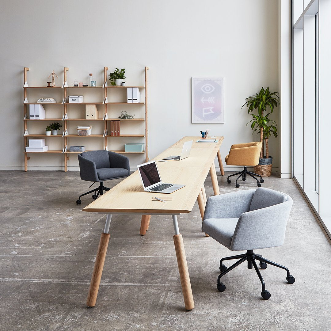 Modern workspace featuring a light wood table, gray and tan chairs, and neutral decor against concrete floors.