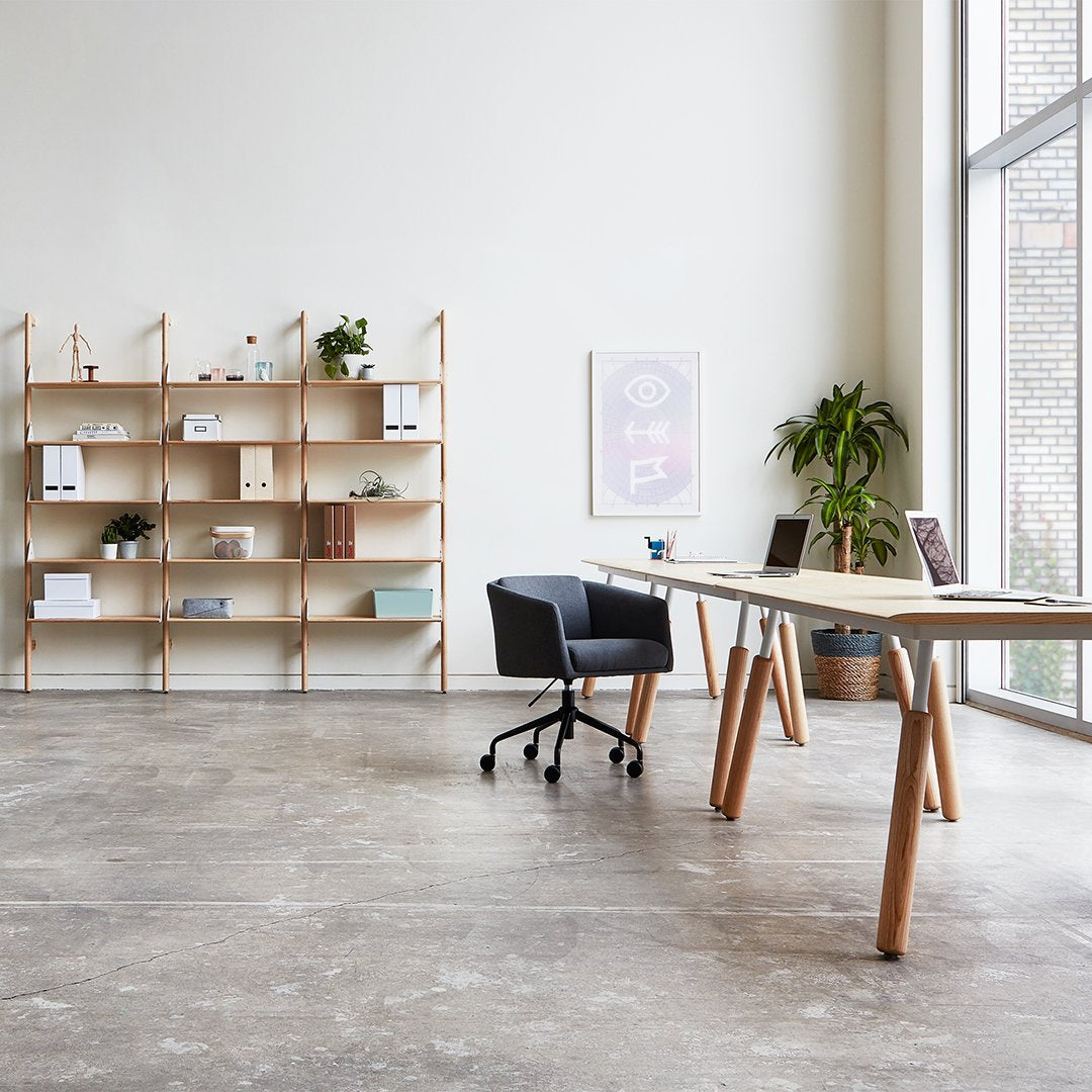 Modern office setup featuring light wood shelving and desk, black office chair, and neutral-toned walls and flooring.