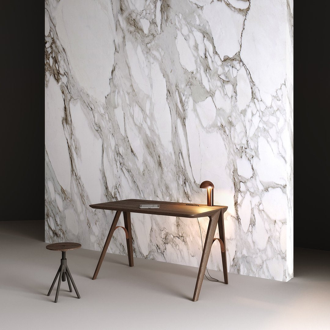 Wooden table with a sleek brown finish against a textured white marble wall featuring grey and gold veining.