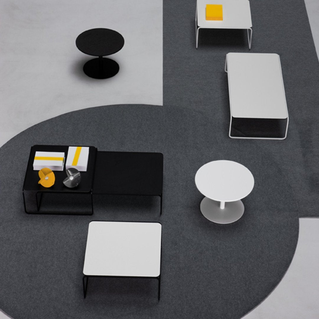 Modern coffee tables in black and white on a sleek gray patterned floor, accented with yellow decor.