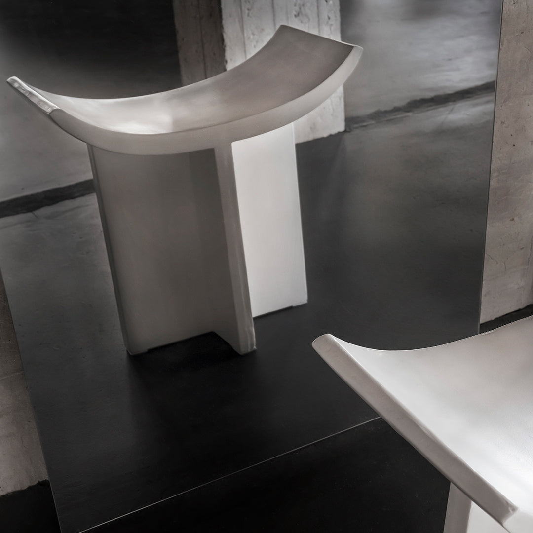 Modern gray stool with a sleek, minimalist design and smooth, polished surface set against a dark background.