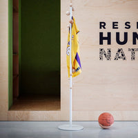 White coat rack with natural wood accents, featuring a vibrant yellow jersey, set against a green wall and gray floor.