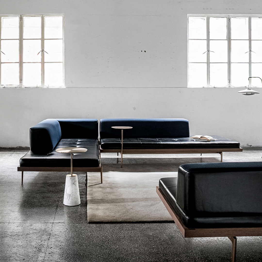 Modern sectional sofa in deep blue and black leather with sleek wooden accents, set against a neutral backdrop.
