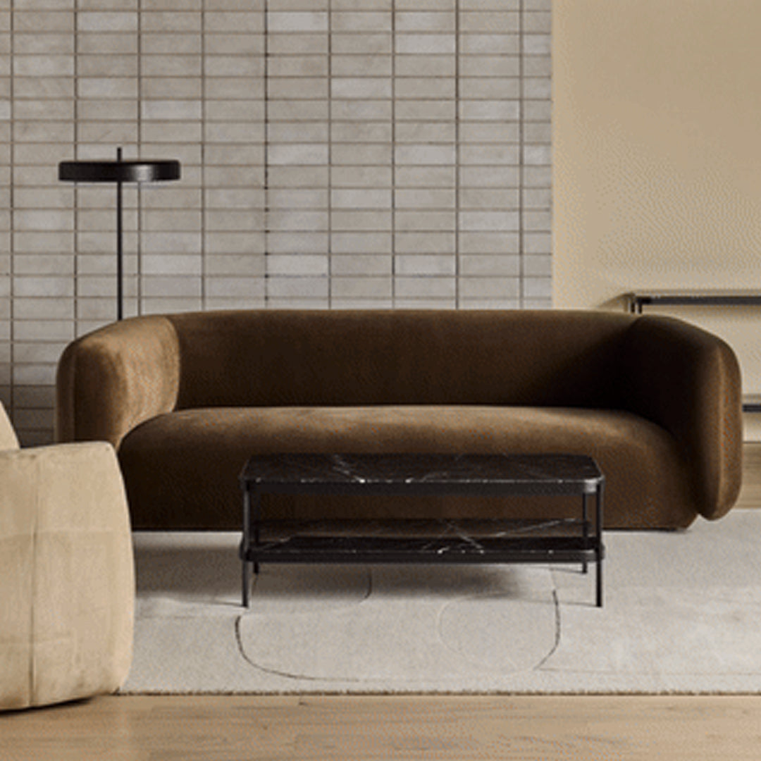 Brown velvet sofa with a sleek curved design, complemented by a black marble coffee table and neutral-toned decor.